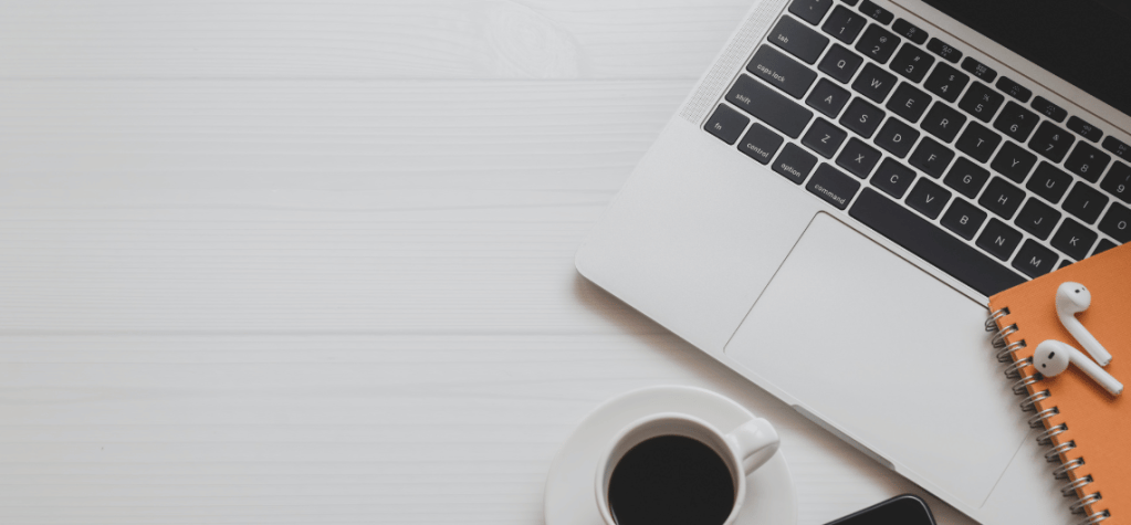 laptop on desk with a cup of coffee and airpods