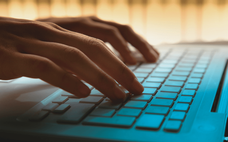 hands typing on laptop keyboard with background lighting